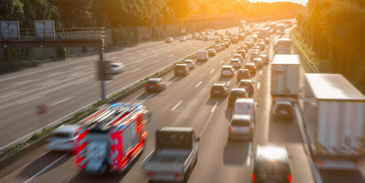 Auf dem Bild ist eine Autobahn mit fahrenden Autos zu sehen. Das Bild ist leicht verschwommen, um die Geschwindigkeit zu symbolisieren.